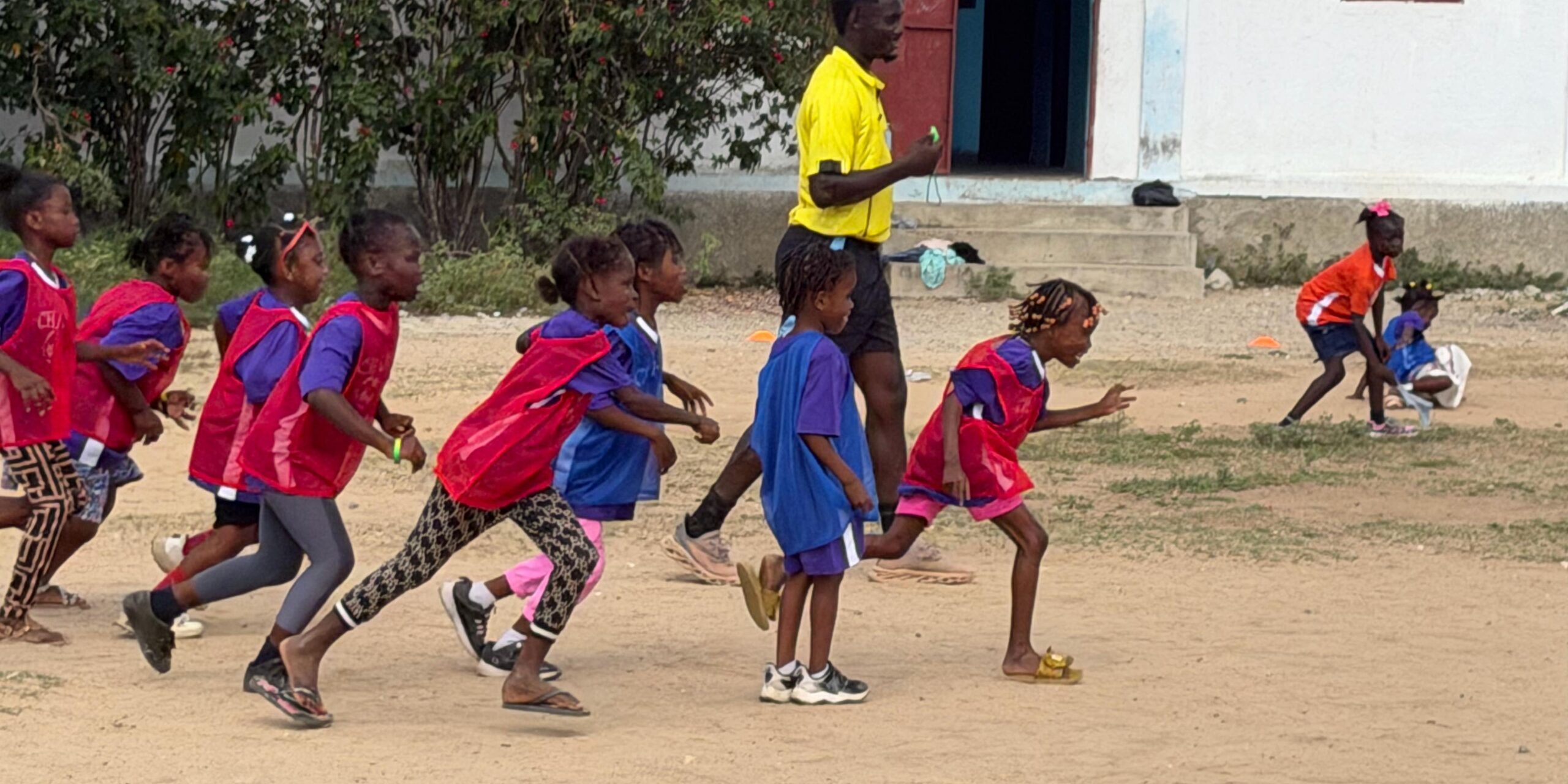 Haitian children in red and blue jerseys running during a youth sports camp drill in Haiti
